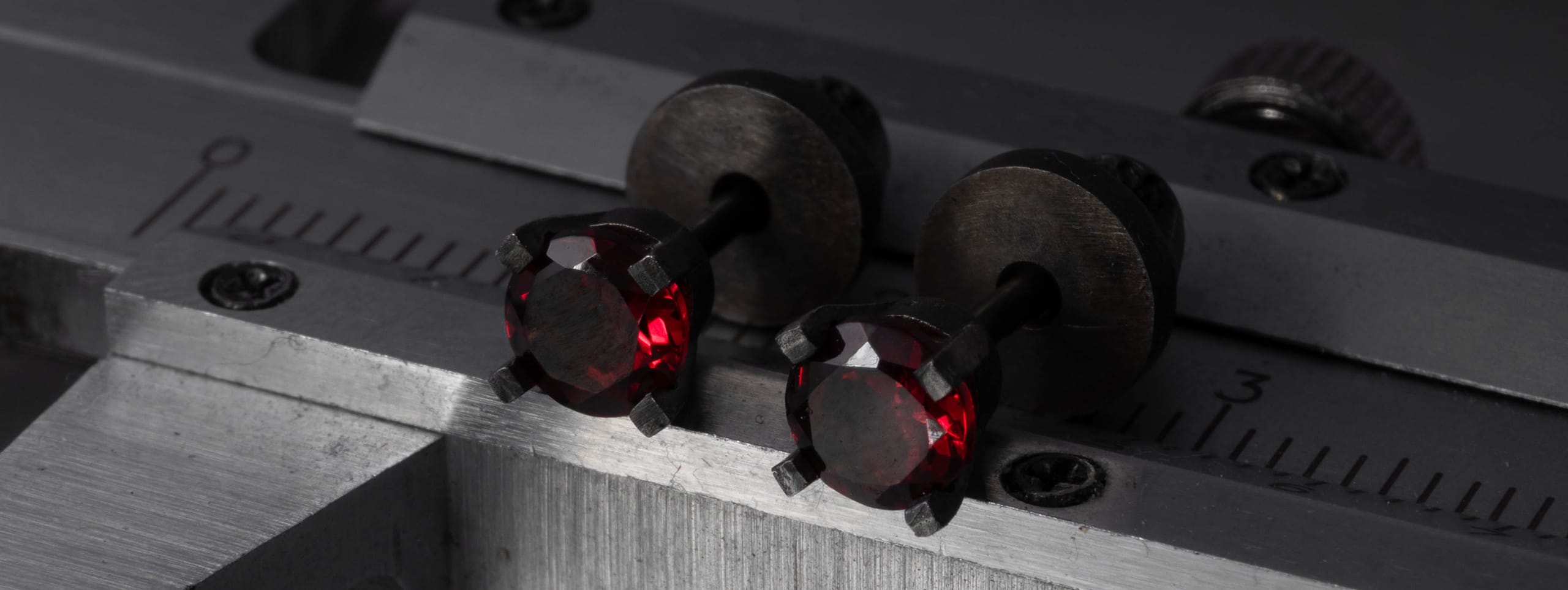 Two CROSS ELEMENTS silver stud earrings with garnet laying on a calipers